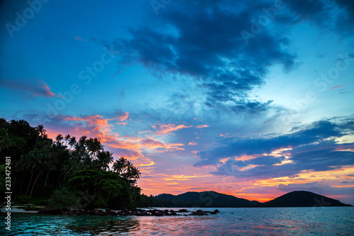 Cloudy Sky burst during sun set with silhouette coconut palm trees over mountain range at Koh Mak Thailand