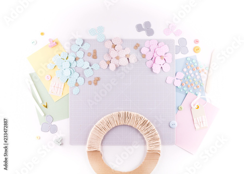 Flat lay, top view craft table desk. Workspace with mat for cutting, scissors, cardstock, paper, pencils on white background. Make floral wreath decor. photo