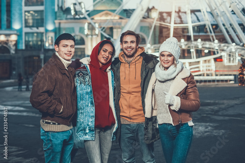 Portrait of satisfied males and cheerful women embracing together while standing outside during winter evening