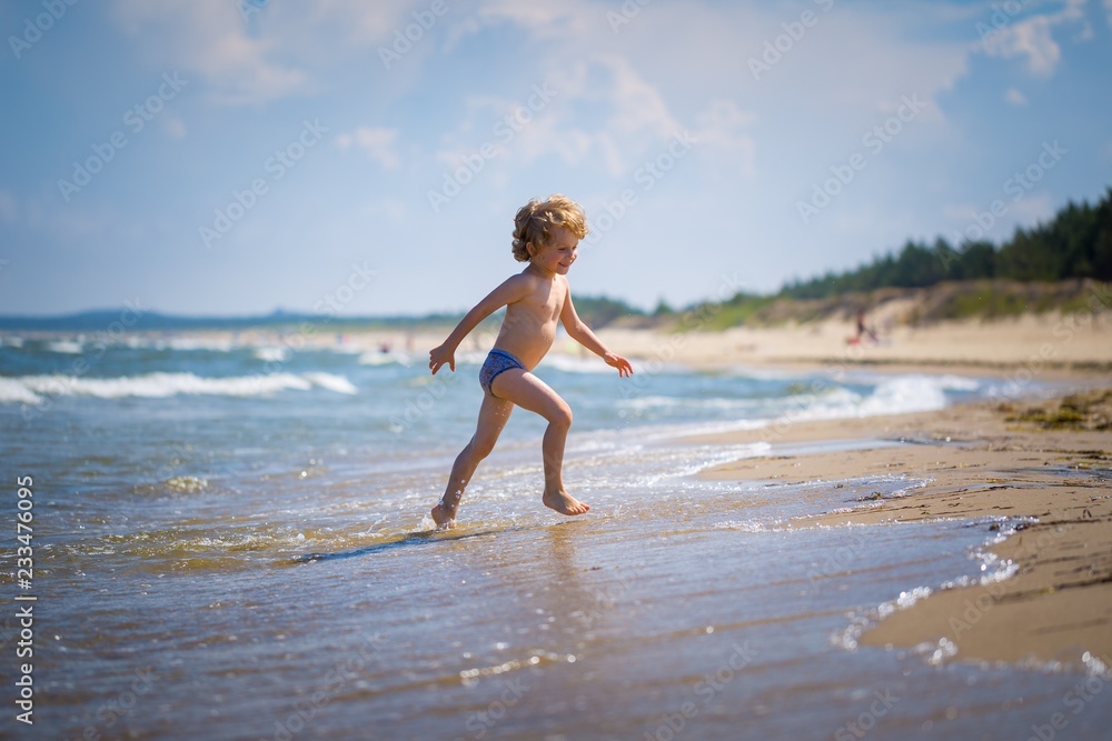 Fototapeta premium Young caucasian boy playing on sea shore at sunny summer