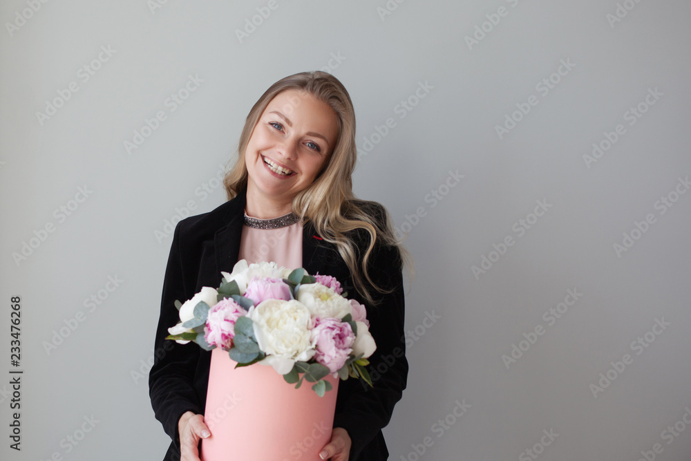 Charming blonde woman with flowers in a hat box. Bouquet of peonies. Girl in business style, receives flowers or gives Charming blonde woman with flowers in a hat box. Bouquet of peonies. Girl in business style, receives flowers or gives