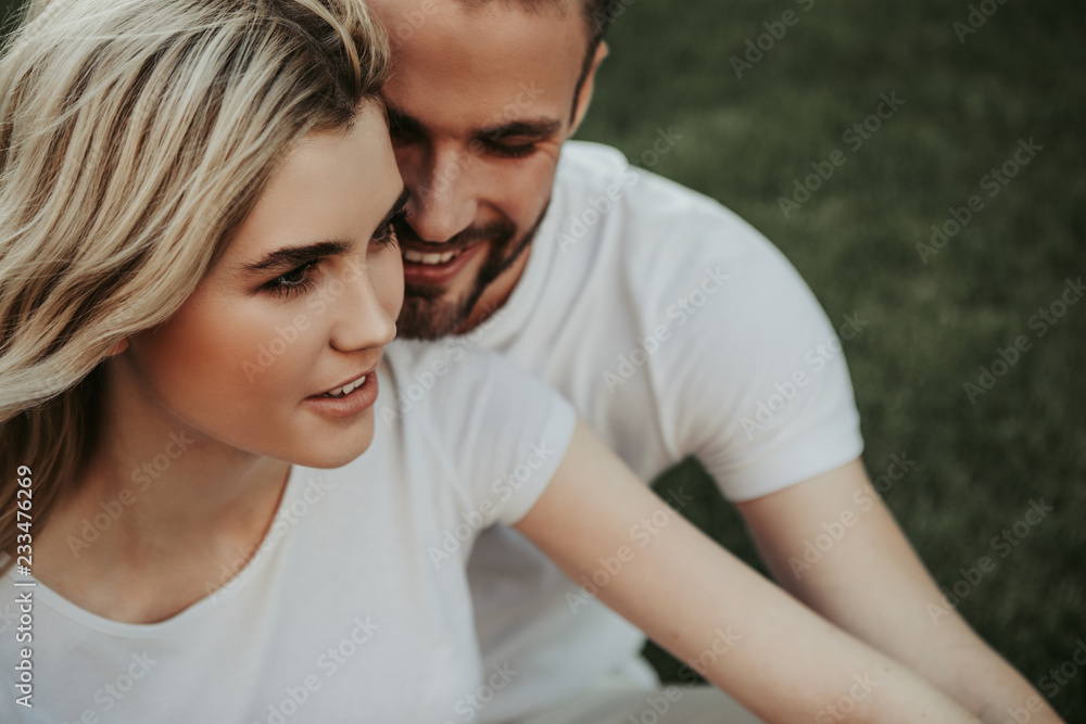 Fototapeta premium Happy interested young man is hugging merry woman while she looking ahead with smile