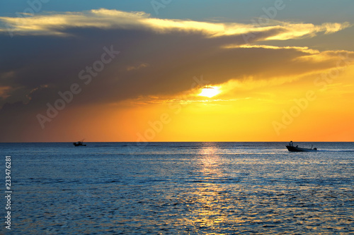 Colorful seascape image with shiny sea and speedboat over cloudy sky and sun during sunset in Cozumel  Mexico