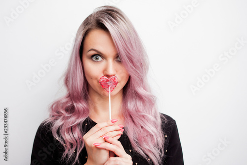 Lovely charming girl with a Lollipop in the form of heart. Portrait of a young woman with pink hair and pink candy
