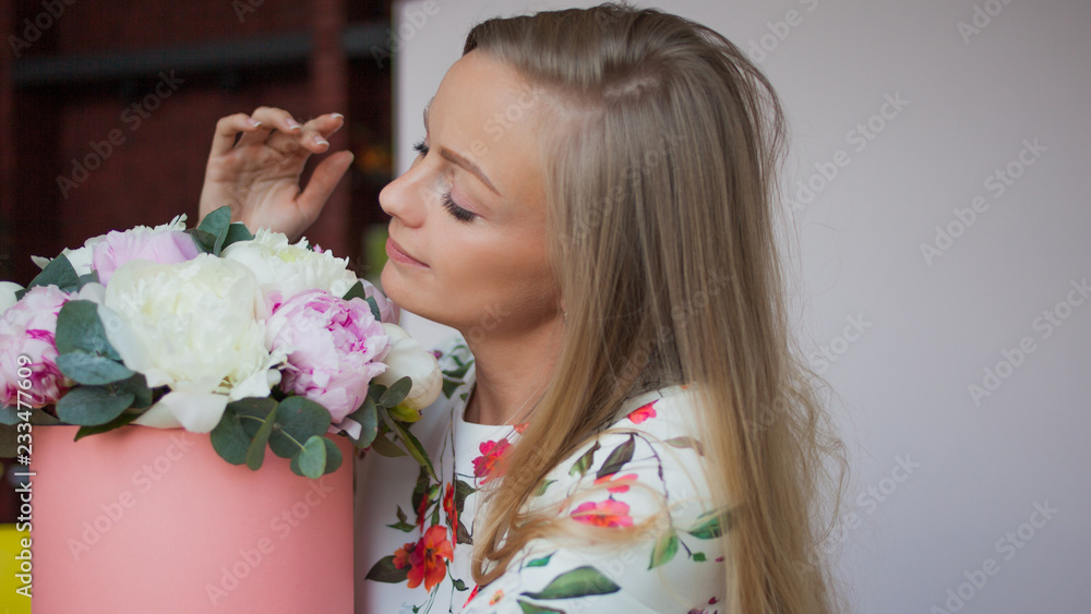 Naklejka premium Happy blonde woman in a modern office with flowers in a hat box. Bouquet of peonies.