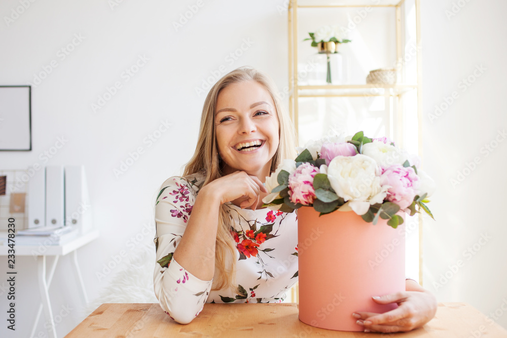 Happy blonde woman in a modern office with flowers in a hat box. Bouquet of peonies. Happy blonde woman in a modern office with flowers in a hat box. Bouquet of peonies.