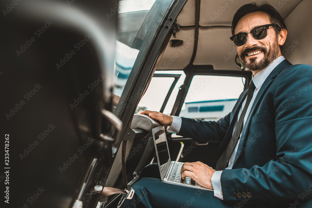 Confident elegant man with modern laptop smiling while sitting in the helicopter Confident elegant man with modern laptop smiling while sitting in the helicopter
