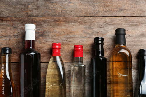 Bottles with different kinds of vinegar and space for text on wooden background, flat lay