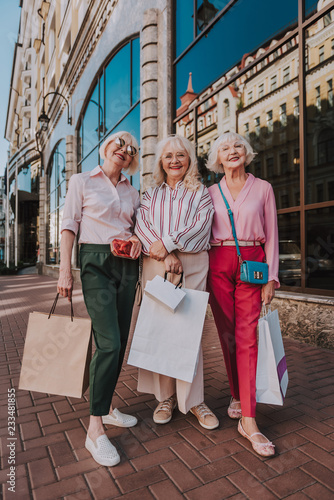 Full-length photo of three happy adult woman walking in the street with shopping bags