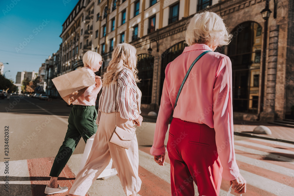 Three stylish older ladies d are going to shopping center while crossing crosswalk