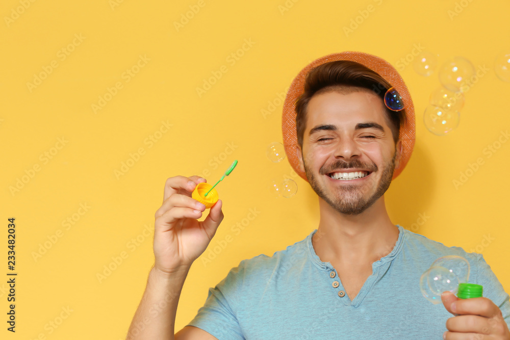Young man blowing soap bubbles on color background. Space for text Young man blowing soap bubbles on color background. Space for text