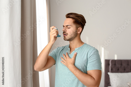 Young man using asthma inhaler at home