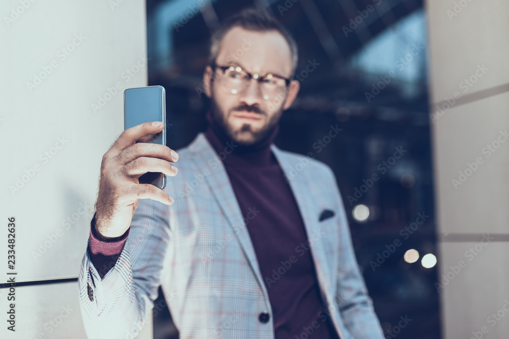 Serious bearded man looking confident while standing in front of the glass and taking photos Serious bearded man looking confident while standing in front of the glass and taking photos