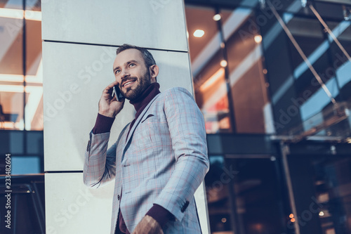 Confident handsome young man standing outdoors with his smartphone and having a pleasant phone talk
