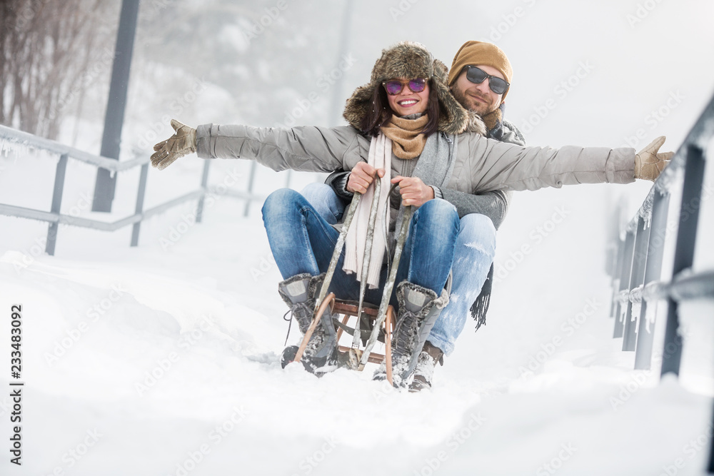 Young couple riding sled in snow - obrazy, fototapety, plakaty 
