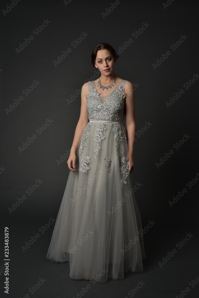 full length portrait of brunette girl wearing long silver ball gown. standing pose on grey studio background. full length portrait of brunette girl wearing long silver ball gown. standing pose on grey studio background.