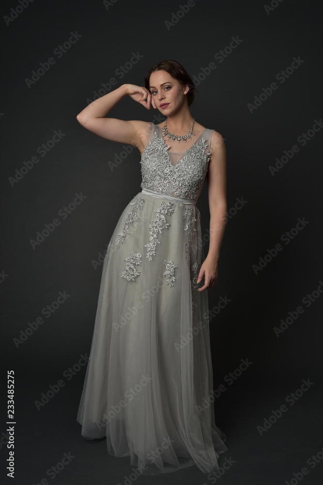 full length portrait of brunette girl wearing long silver ball gown. standing pose on grey studio background. full length portrait of brunette girl wearing long silver ball gown. standing pose on grey studio background.