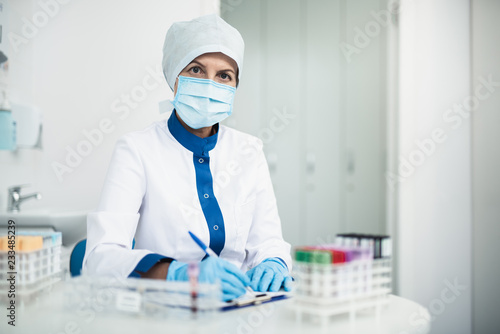 Professional facility investigations in healthcare system. Waist up portrait of female laboratory expert making notes at lab office. Copy space on right photo