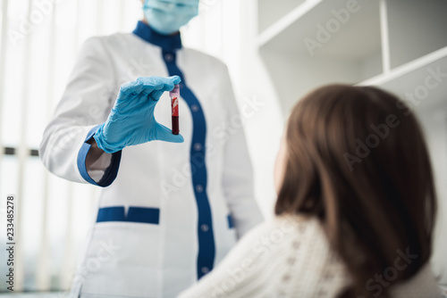 Professional facility investigations in healthcare system. Low angle waist up portrait of female laboratory worker showing test tube with blood to little girl