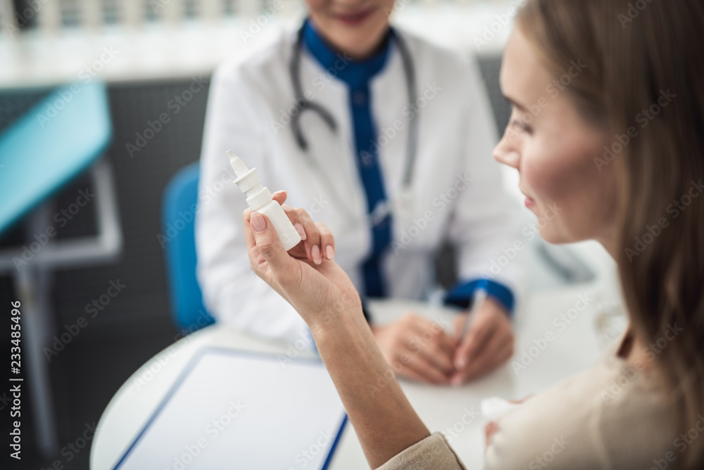 Concept of professional consultation and remedy. Close up portrait of young female patient with running nose holding nasal drops while staying medical office Concept of professional consultation and remedy. Close up portrait of young female patient with running nose holding nasal drops while staying medical office