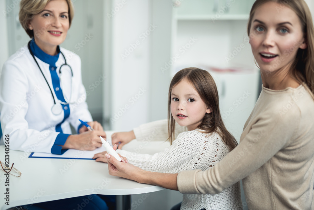 Concept of professional consultation in therapist practice. Waist up portrait of surprised young woman with daughter taking bottle of nasal drops from pediatrician Concept of professional consultation in therapist practice. Waist up portrait of surprised young woman with daughter taking bottle of nasal drops from pediatrician