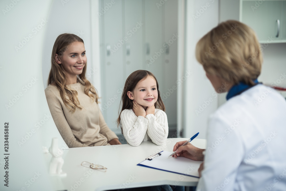 Concept of therapist consultation in healthcare system. Waist up back side portrait of pediatrician woman making notes while consulting mother and her daughter Concept of therapist consultation in healthcare system. Waist up back side portrait of pediatrician woman making notes while consulting mother and her daughter