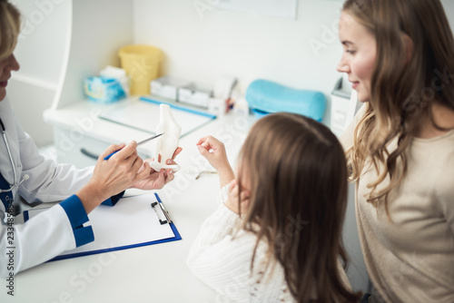 Concept of positive therapist consultation in healthcare system. Close up portrait of pediatrician woman showing medical model of knee joint to little girl and her mother