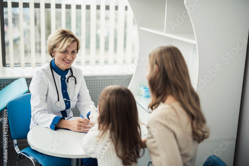 Concept of positive therapist consultation in healthcare system. Waist up portrait of smiling pediatrician woman making notes while consulting little girl and her mother