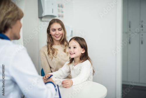 Concept of professional consultation in healthcare system. Waist up portrait of pediatrician woman consulting mother and her cheerful daughter in practice office