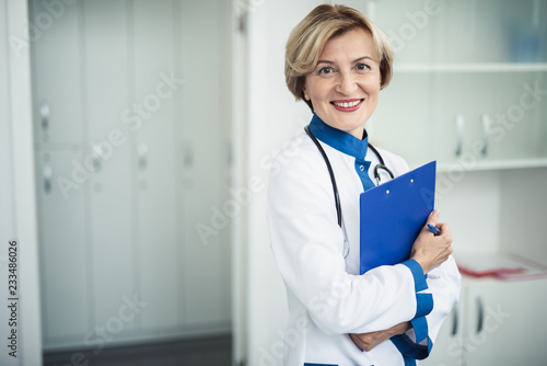 Concept of professional inspiration in healthcare system. Waist up portrait of smiling female doctor standing in medical cabinet with note holder. Copy space on left