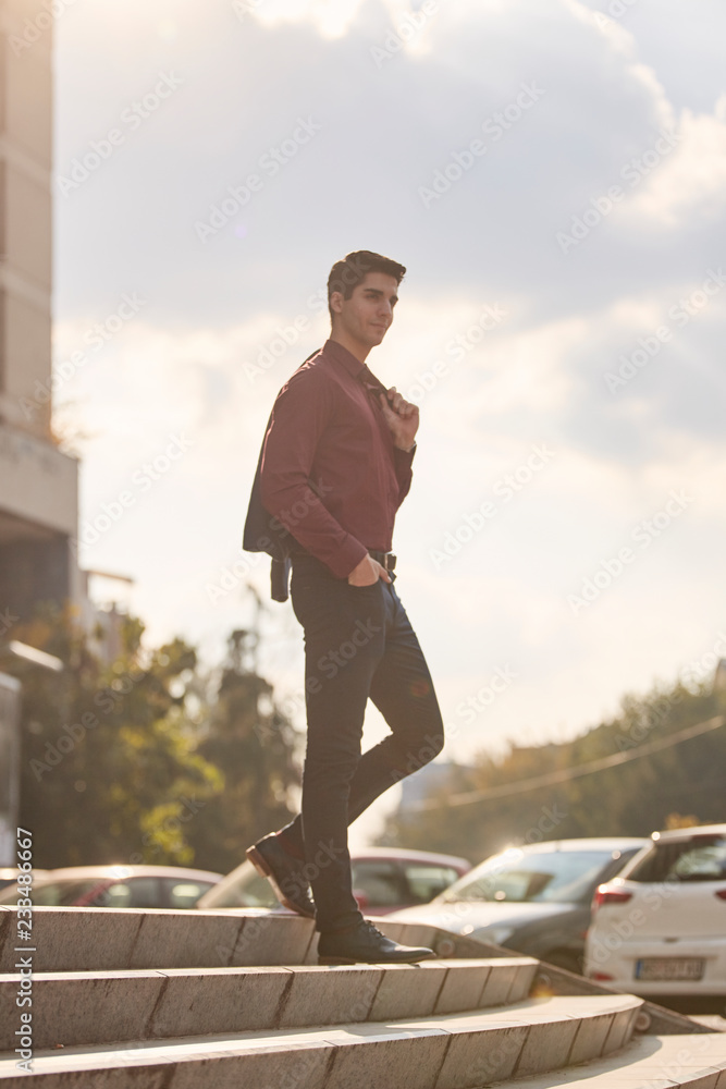 one young man, standing posing on steps, wearing suit. sunny day outdoors, sky and cars behind. one young man, standing posing on steps, wearing suit. sunny day outdoors, sky and cars behind.
