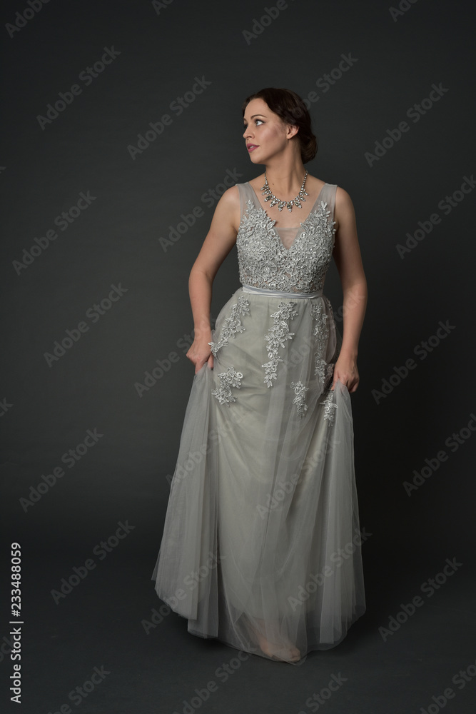 full length portrait of brunette girl wearing long silver ball gown. standing pose on grey studio background. full length portrait of brunette girl wearing long silver ball gown. standing pose on grey studio background.