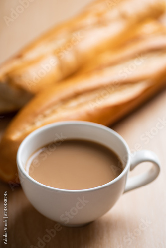 Cup of coffee and baguette french bread on wooden table in the morning