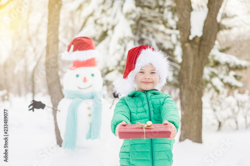 smiling boy in red christmas hat holds gift box with snowman on background