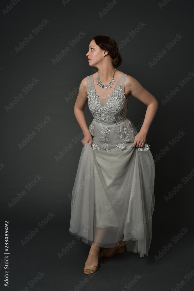 full length portrait of brunette girl wearing long silver ball gown. standing pose on grey studio background. full length portrait of brunette girl wearing long silver ball gown. standing pose on grey studio background.