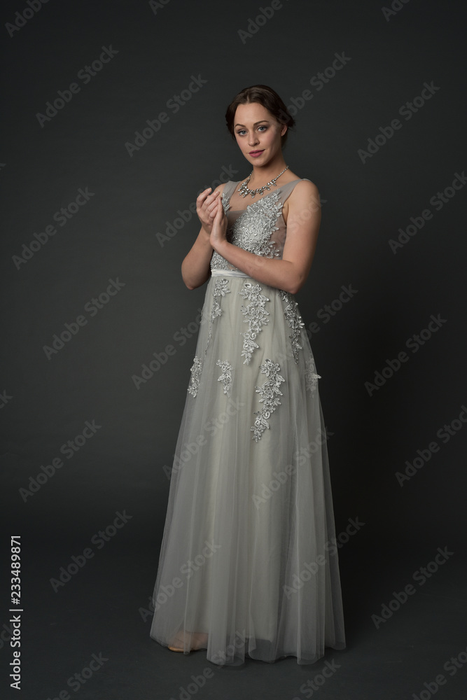 full length portrait of brunette girl wearing long silver ball gown. standing pose on grey studio background. full length portrait of brunette girl wearing long silver ball gown. standing pose on grey studio background.
