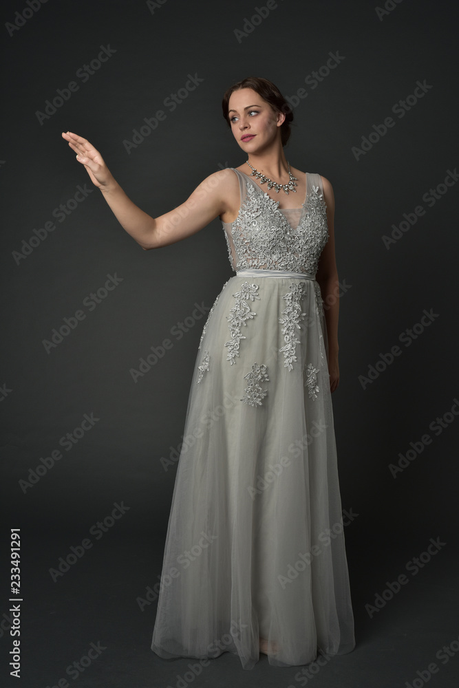 full length portrait of brunette girl wearing long silver ball gown. standing pose on grey studio background. full length portrait of brunette girl wearing long silver ball gown. standing pose on grey studio background.