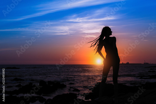 Silhouette of a young joyful woman on the sea beach at amazing sunset. © De Visu