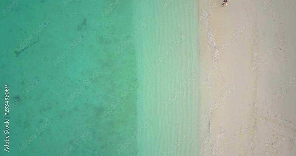 Top down overhead stationary aerial view of person walking on white sand beach, waves lapping from clear emerald green sea on tropical island in Thailand. 4k 1.9:1 23.976fps Top down overhead stationary aerial view of person walking on white sand beach, waves lapping from clear emerald green sea on tropical island in Thailand. 4k 1.9:1 23.976fps