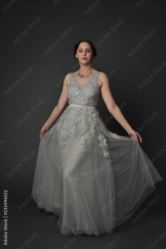 full length portrait of brunette girl wearing long silver ball gown. standing pose on grey studio background. full length portrait of brunette girl wearing long silver ball gown. standing pose on grey studio background.