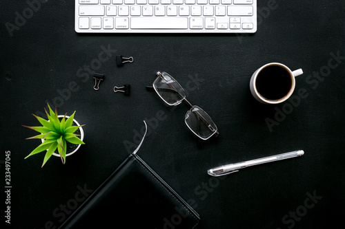 Flat lay of office desk, office workplace. Keyboard and glasses near coffee and stationery on black background top view