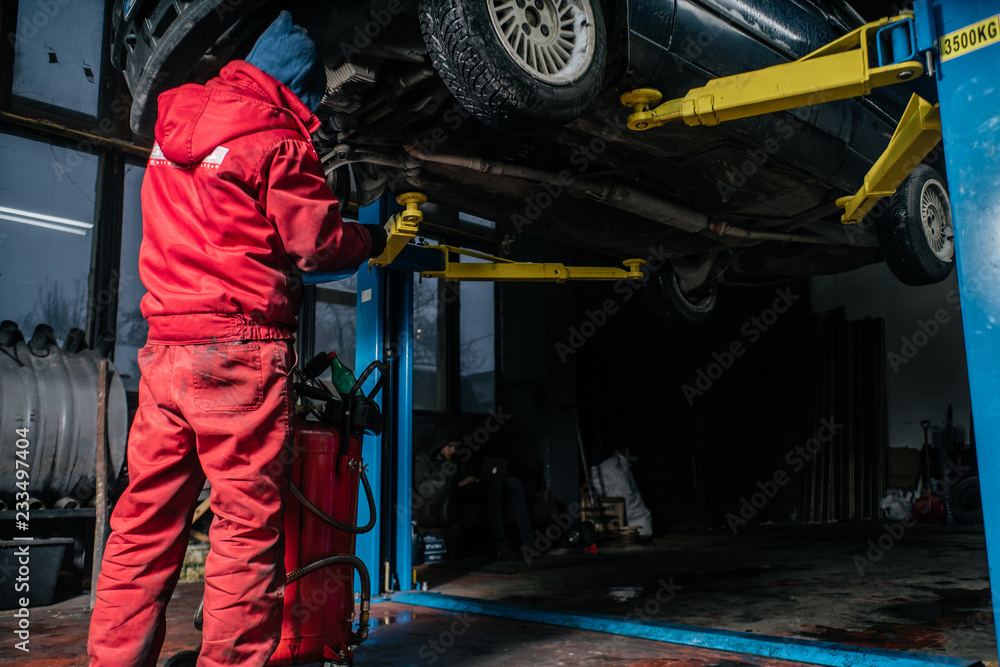 Young caucasian man in red work clothing repairing car with professional tools
