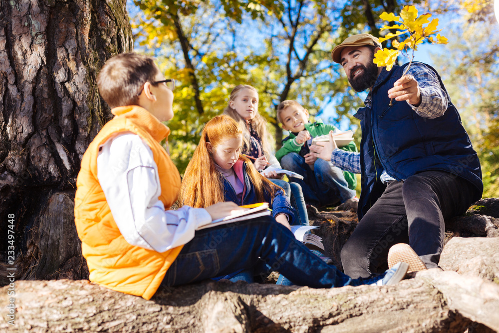 © zinkevych - Nature exploration. Positive bearded man sitting in front of kids while holding a tree branch in front of him