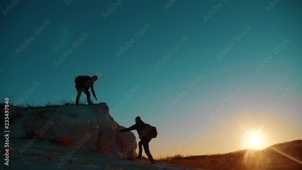 Teamwork tourists. friendship hiking help each other trust assistance silhouette in mountains. Backpacker helps to his friend to climb to rock. two travelers help stretching hand. tourist victory Teamwork tourists. friendship hiking help each other trust assistance silhouette in mountains. Backpacker helps to his friend to climb to rock. two travelers help stretching hand. tourist victory