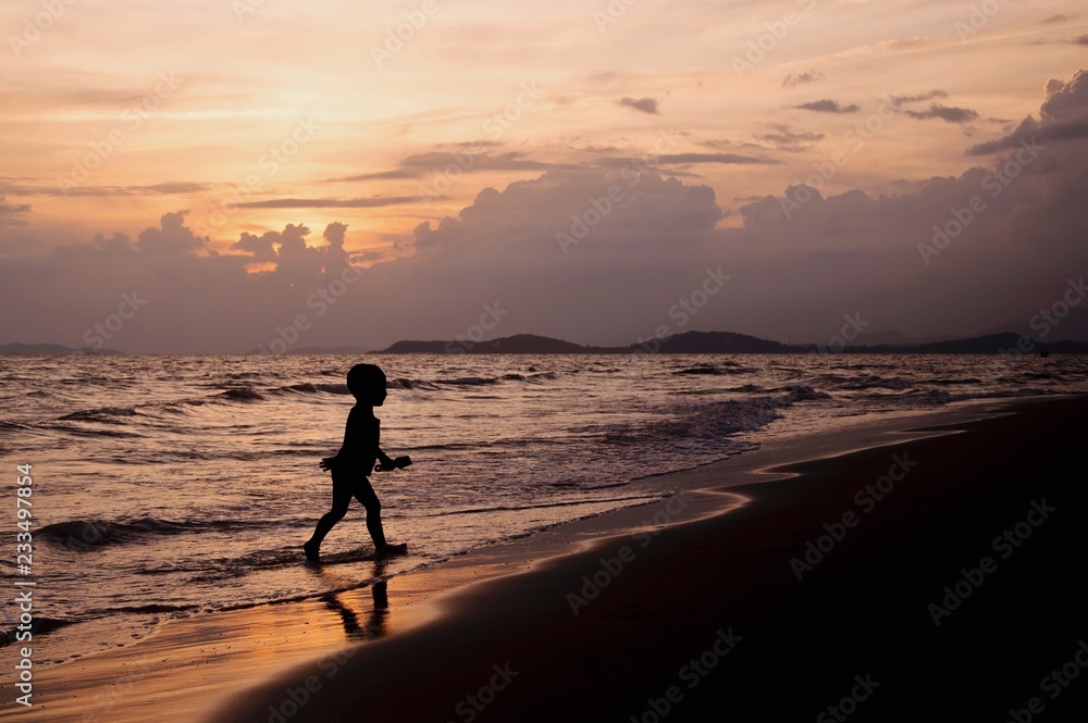 Silhouette of boy playing on the beach with sunset sky