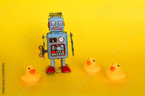 Vintage tin toy robot and small ducklings isolated on a yellow background.