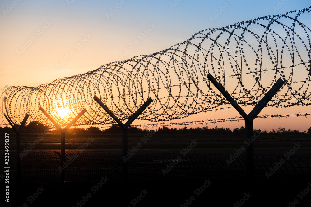 Silhouette of a barbed wire fence steel jail with the sunset in the background Silhouette of a barbed wire fence steel jail with the sunset in the background