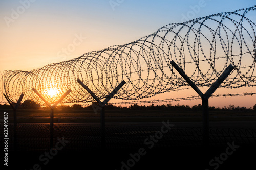 Silhouette of a barbed wire fence steel jail  with the sunset in the background