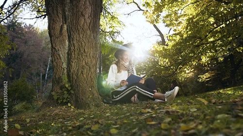 Stylish girl in the hat relaxing in the park, reading book while sitting on the grass. photo