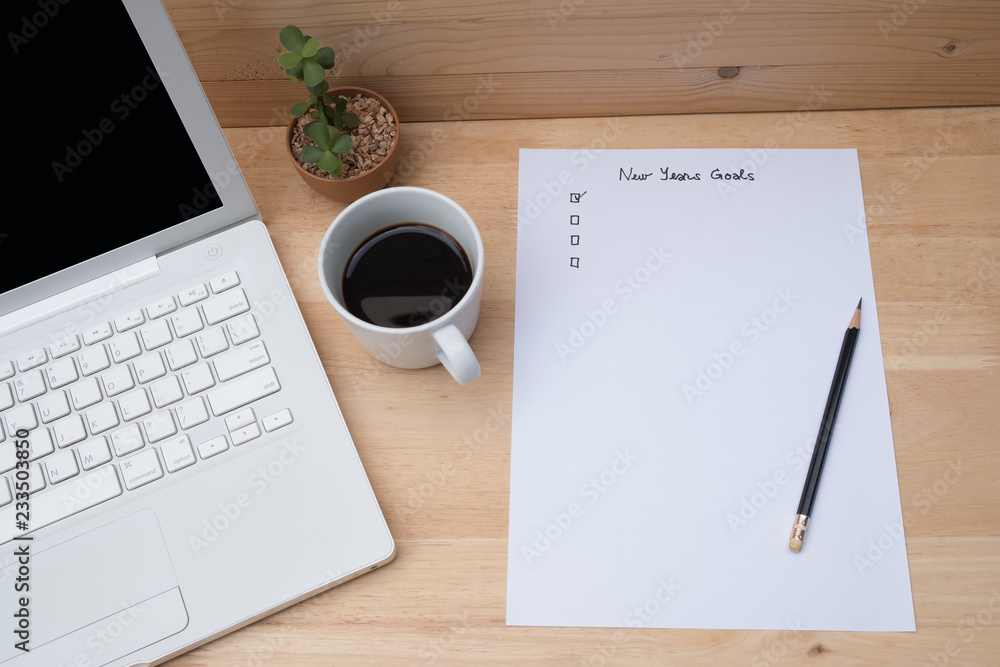 Paper check list for new year goals, laptop, coffee on wooden table. Planning work for new year. Paper check list for new year goals, laptop, coffee on wooden table. Planning work for new year.